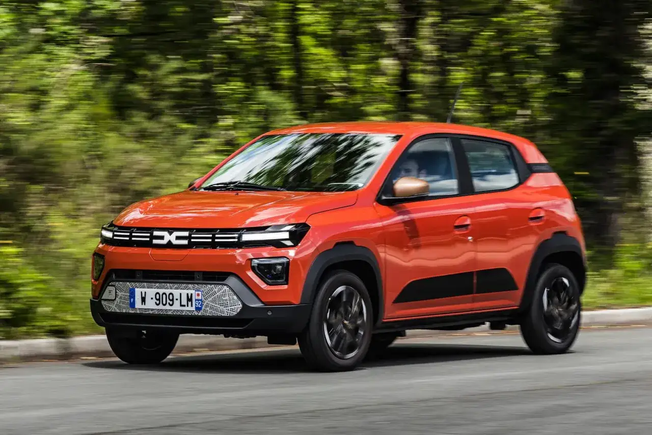 Dacia Spring arancione in movimento, la sua compatta lunghezza la rende ideale per la città.