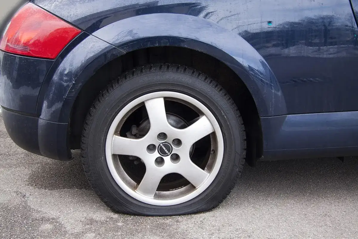 Ruota posteriore di un'auto blu con evidente perdita pressione pneumatici. Il battistrada è schiacciato sull'asfalto.