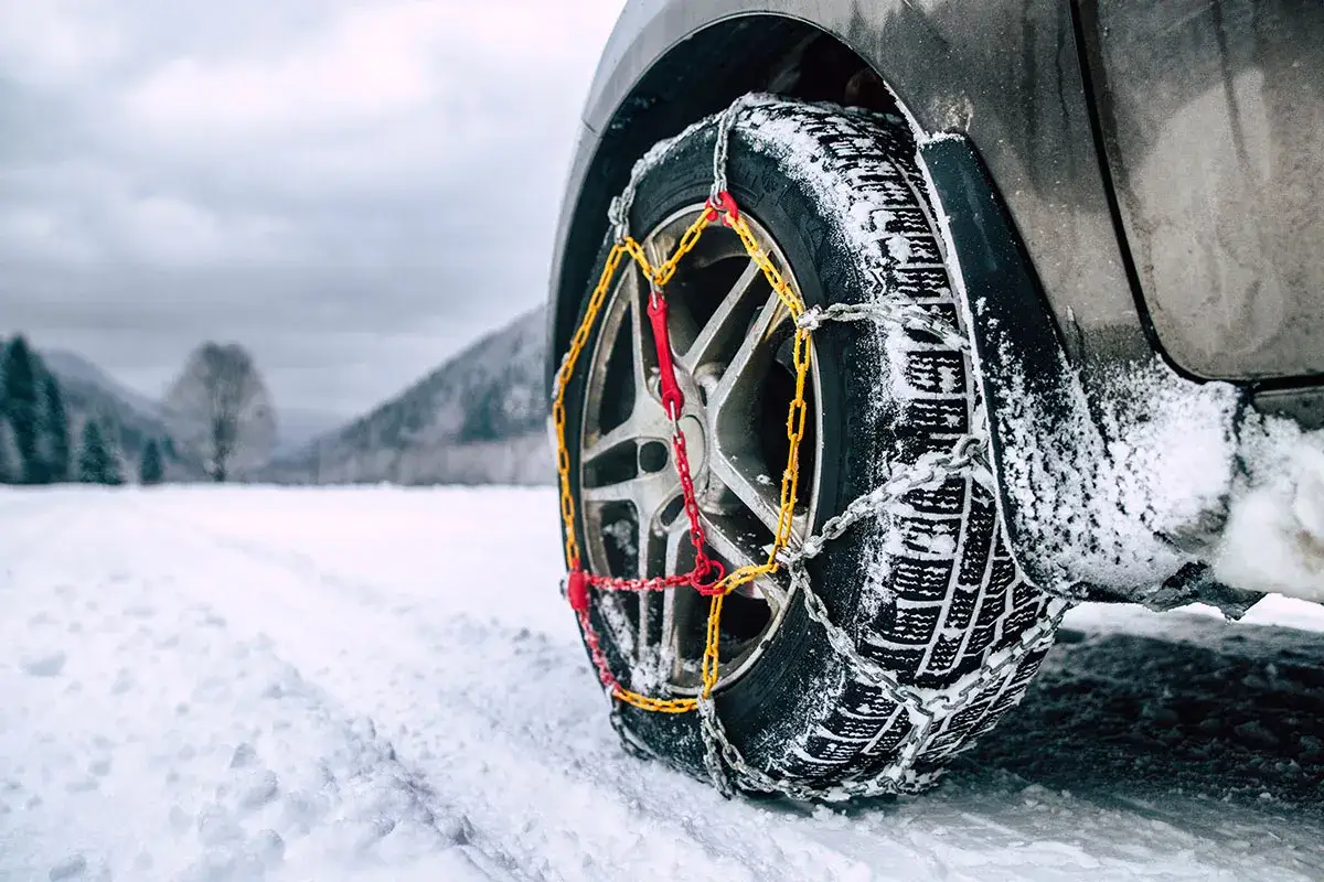 Catene da neve senza codice: come riconoscerle. Ruota di un'auto con catene montate su strada innevata.