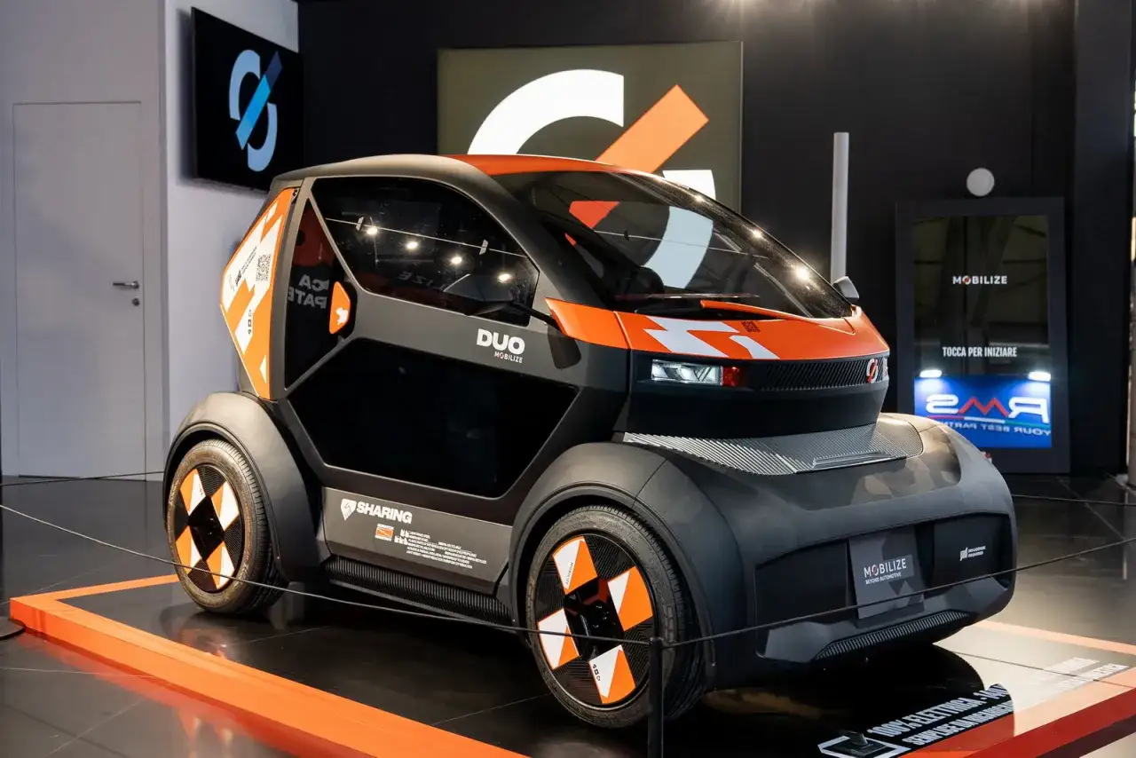 Un'agile auto elettrica due posti, la DUO MOBILIZE, con dettagli arancioni e neri, pronta per il car sharing urbano.