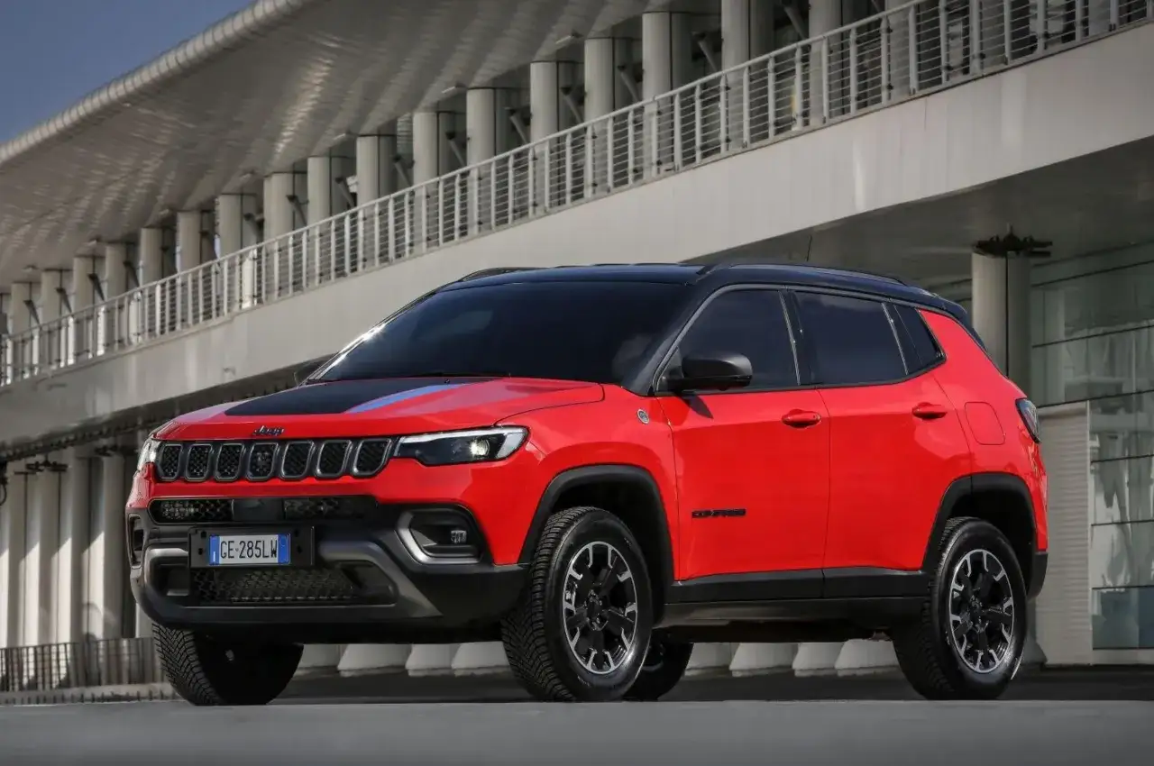 Jeep Compass 1.6 diesel rossa, con tetto nero, parcheggiata davanti a un edificio moderno. Nessun difetto visibile.