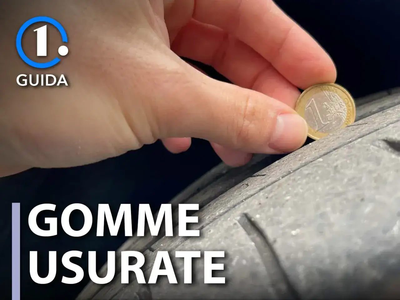 Una mano tiene una moneta da 1 euro per controllare l'usura del battistrada di uno pneumatico. La spalla pneumatico è visibilmente consumata.