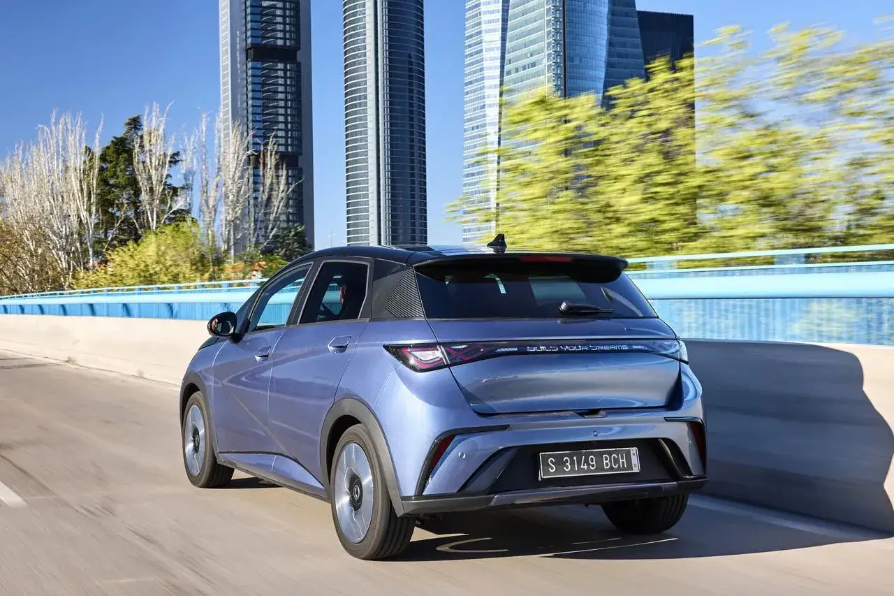 Auto elettriche più vendute: una berlina blu metallizzato sfreccia su un ponte con grattacieli sullo sfondo.