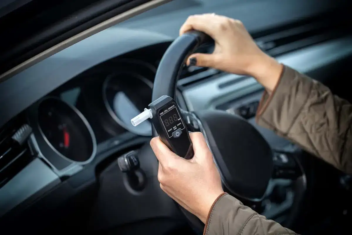 Mani al volante, un dispositivo alcolock in mano per un viaggio sicuro.