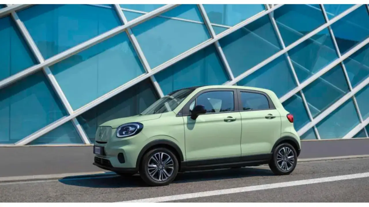 Una moderna auto utilitaria color pistacchio parcheggiata davanti a un edificio con vetri blu e una struttura geometrica bianca.