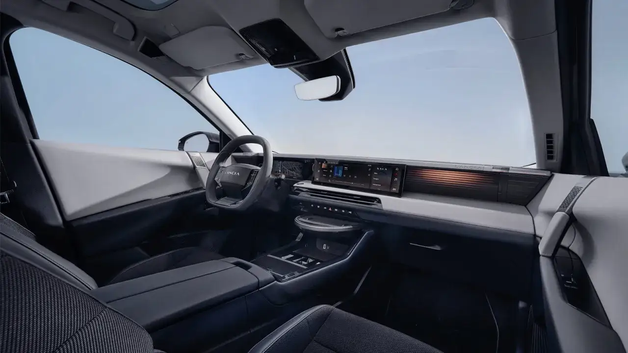 Interni moderni e minimalisti dell'abitacolo di un'auto, con un grande schermo centrale e il logo Lancia che anticipa la lancia gamma 2026.