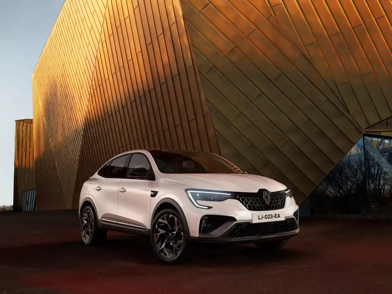 Un bianco SUV coupé Renault, uno dei nuovi modelli, si staglia contro un edificio moderno con rivestimenti dorati.