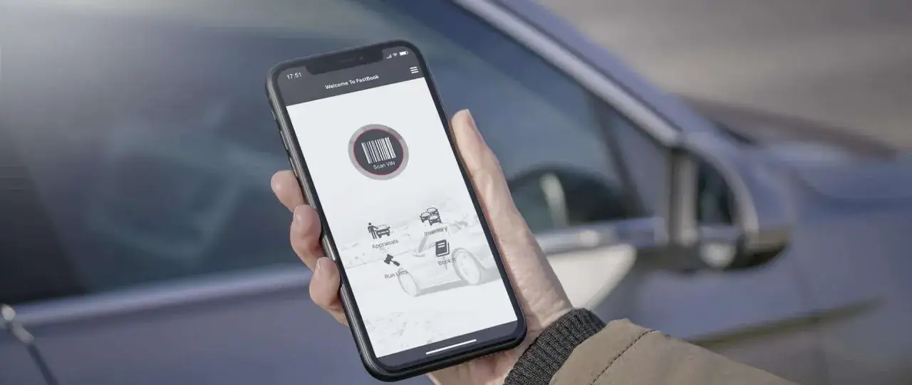 Mano che tiene uno smartphone con l'app FastBook aperta, pronta per scansionare il VIN di un'auto. Ottimo per la gestione del tuo autobiz.