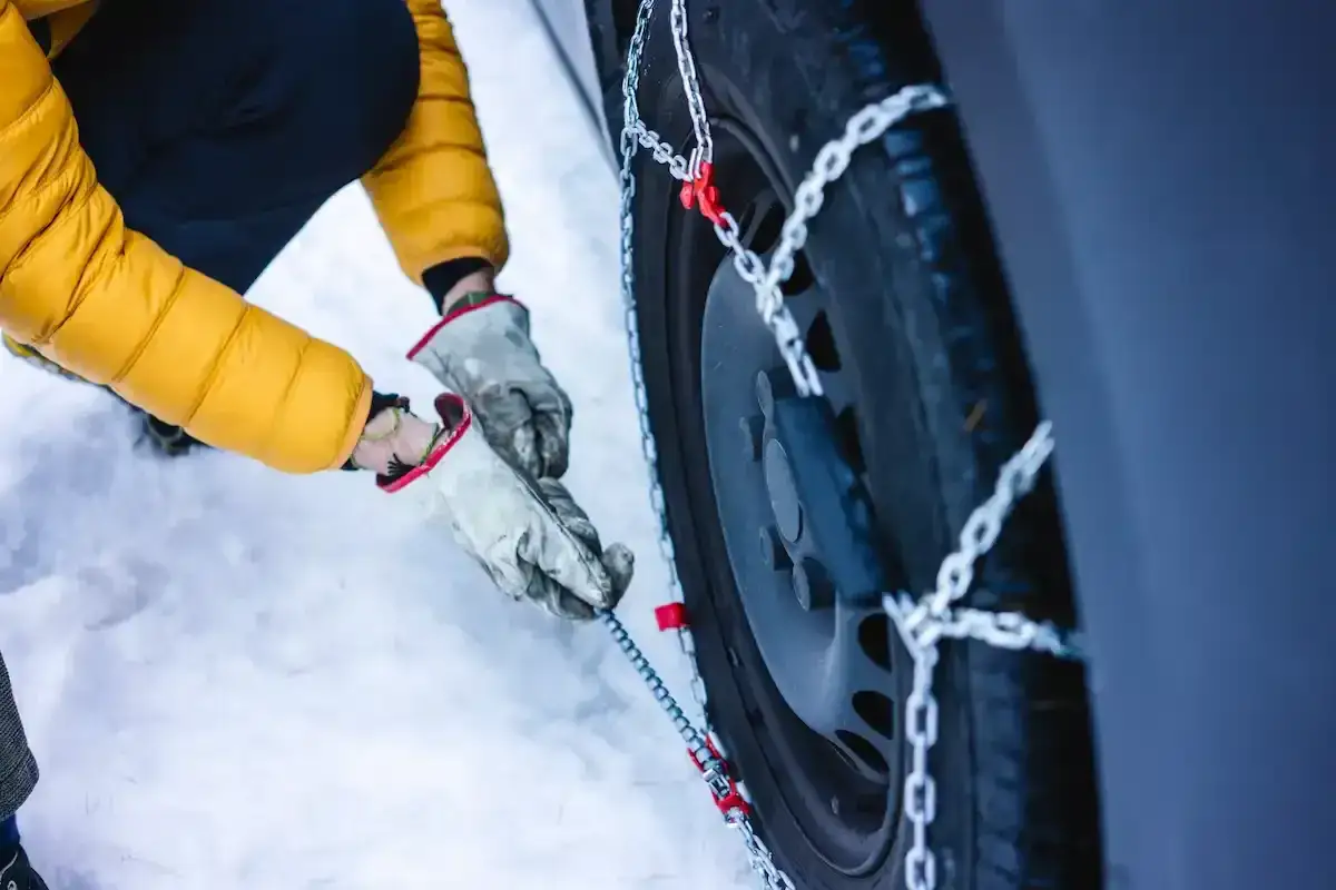Mani guantate montano le catene da neve su una gomma 4 stagioni. Anche se le gomme sono adatte a tutte le stagioni, se ho le gomme 4 stagioni devo avere le catene per la sicurezza sulla neve.