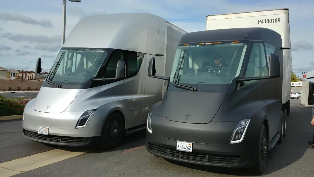 Due camion Tesla, uno argento e uno nero, parcheggiati uno accanto all'altro. Il camioncino nero ha un conducente all'interno. Il camion Tesla prezzo è un argomento di grande interesse.