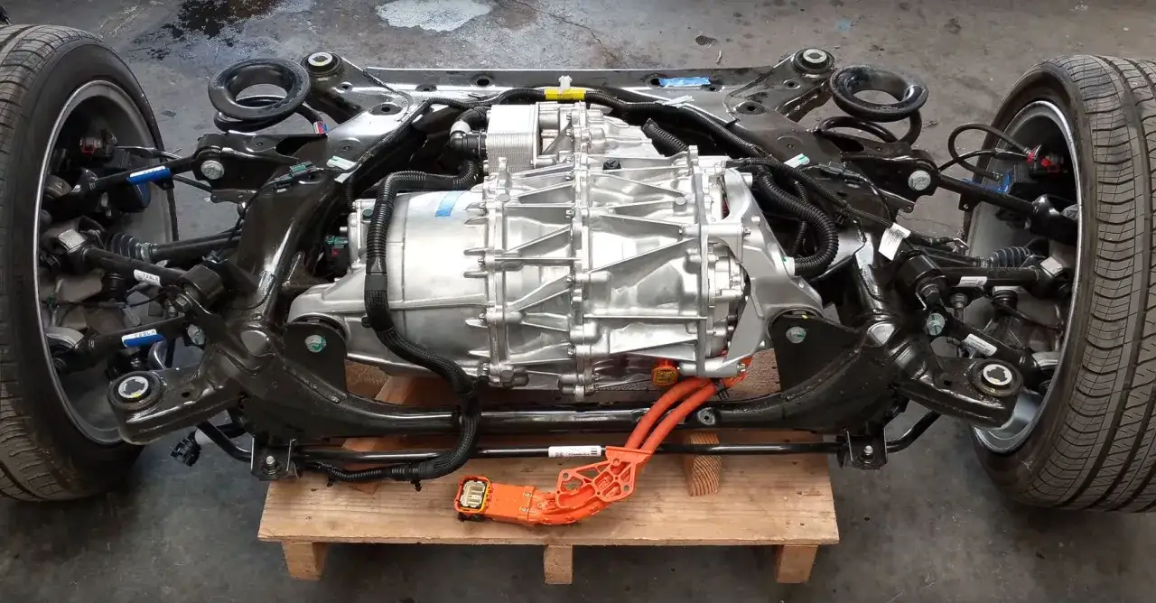 Il motore Tesla, parte di un telaio con ruote, sospensioni e cavi arancioni, pronto per essere installato.