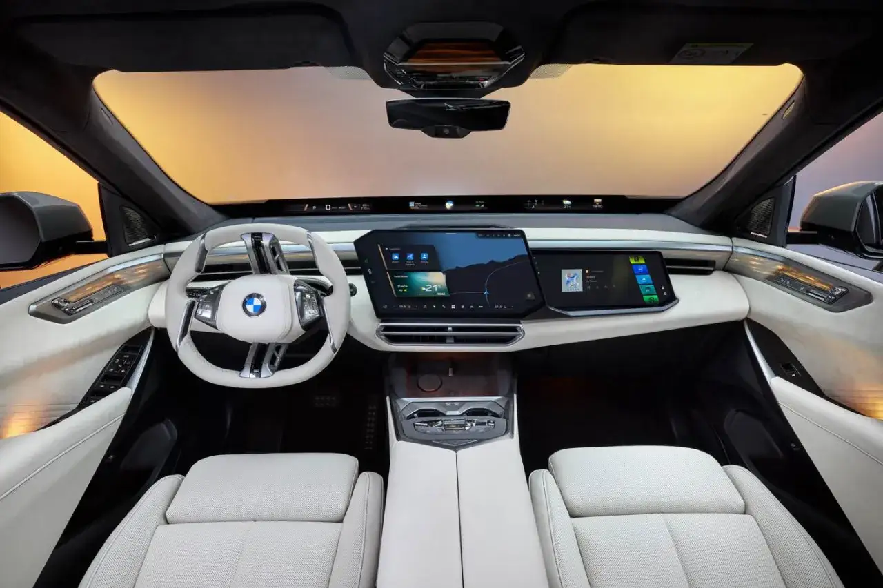 Interni lussuosi del BMW X5 2026 con schermi digitali, volante moderno e sedili in pelle chiara.