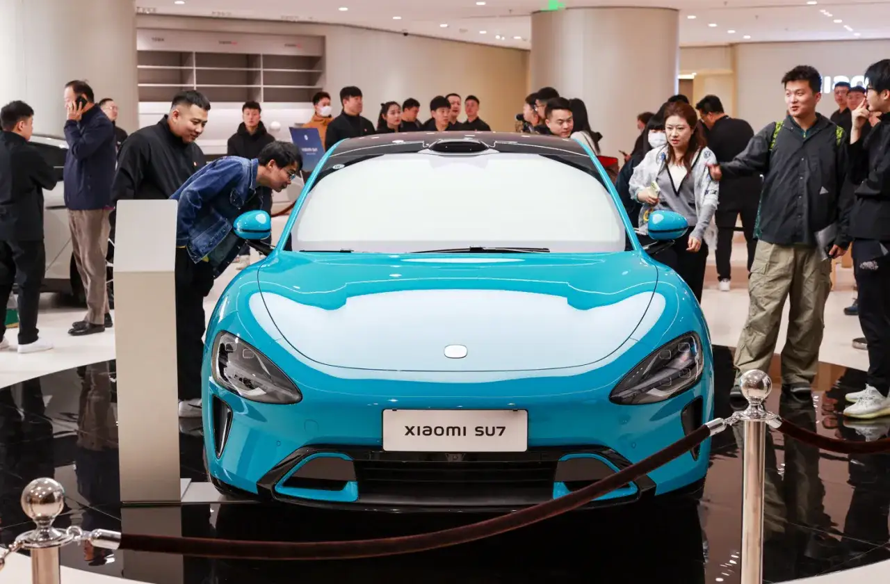 Un'auto Xiaomi SU7 blu brillante in esposizione, circondata da curiosi.