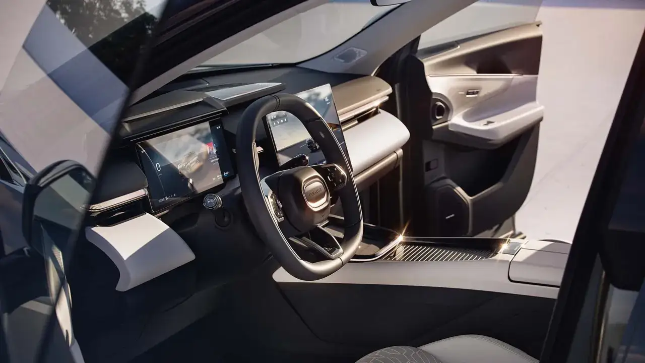Interno moderno di un'auto con schermi digitali e volante. Il logo 
