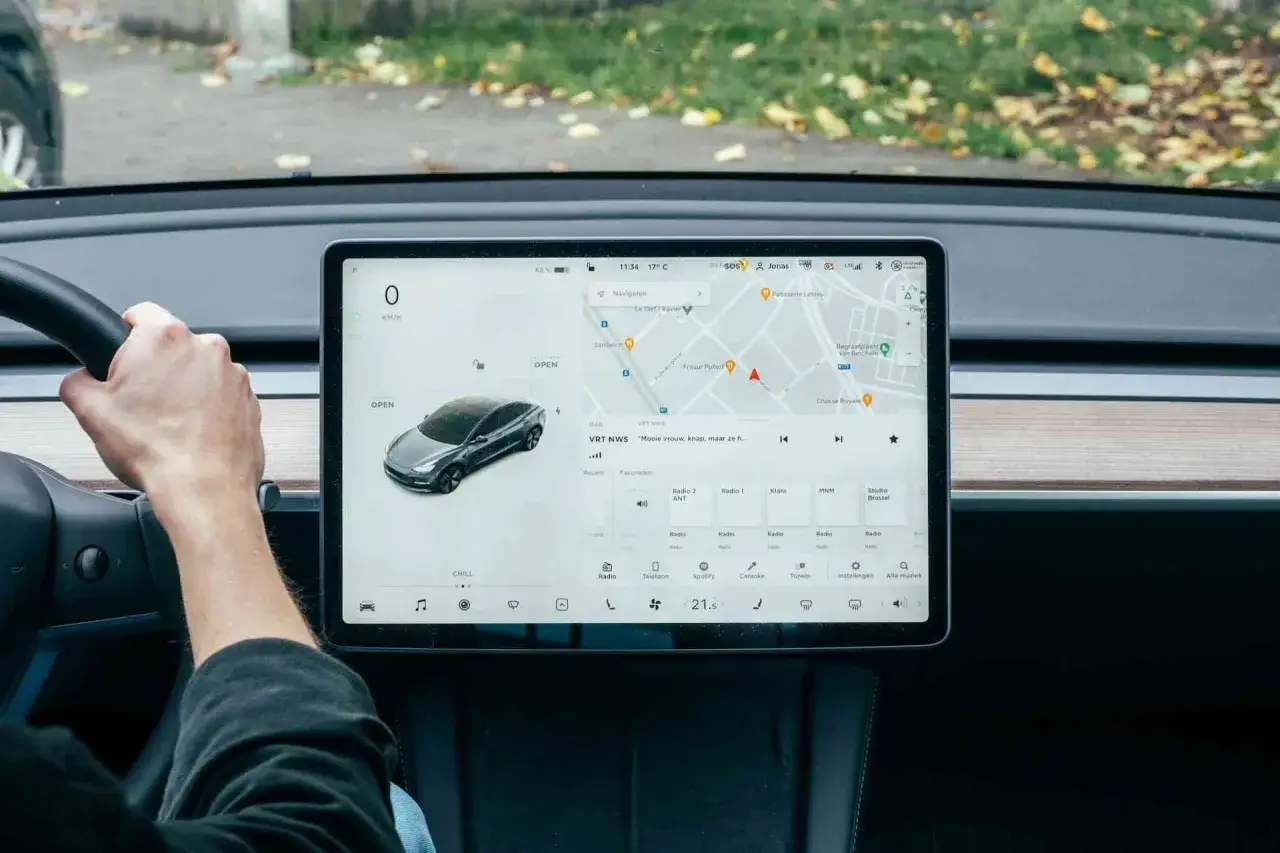 Interno di una Tesla con schermo touch che mostra navigazione e radio. L'interfaccia ricorda Apple CarPlay per la sua intuitivit&agrave;.