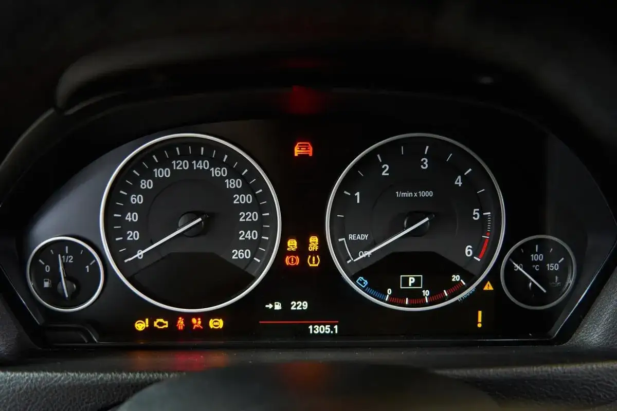 Cruscotto auto con spie accese, tra cui quella di avaria motore e gomme sgonfie. Il tachimetro indica 0 km/h.