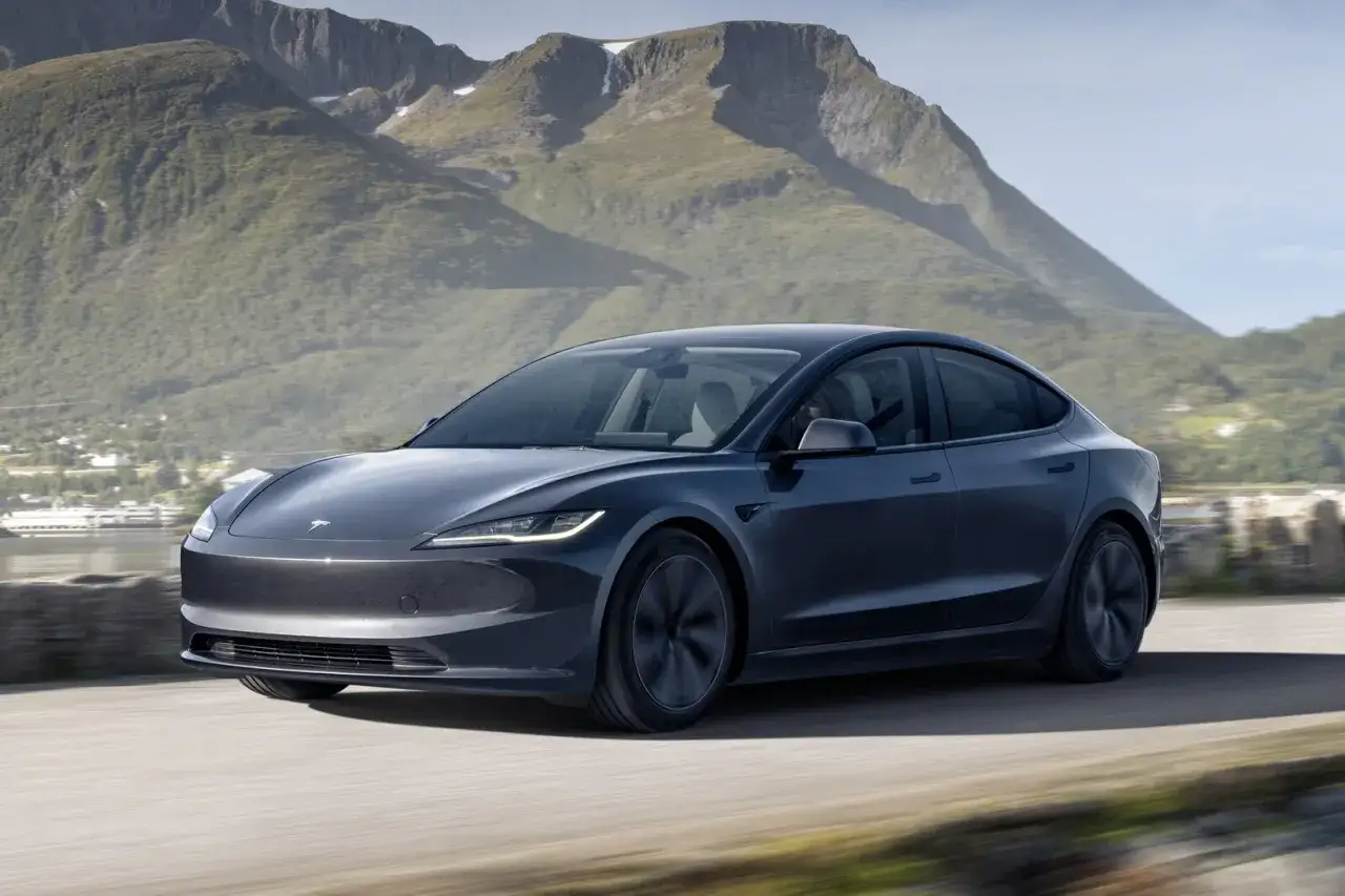 Tesla Model 3 grigia in movimento su strada panoramica, con montagne sullo sfondo. La tecnologia Tesla FSD promette un futuro di guida autonoma.