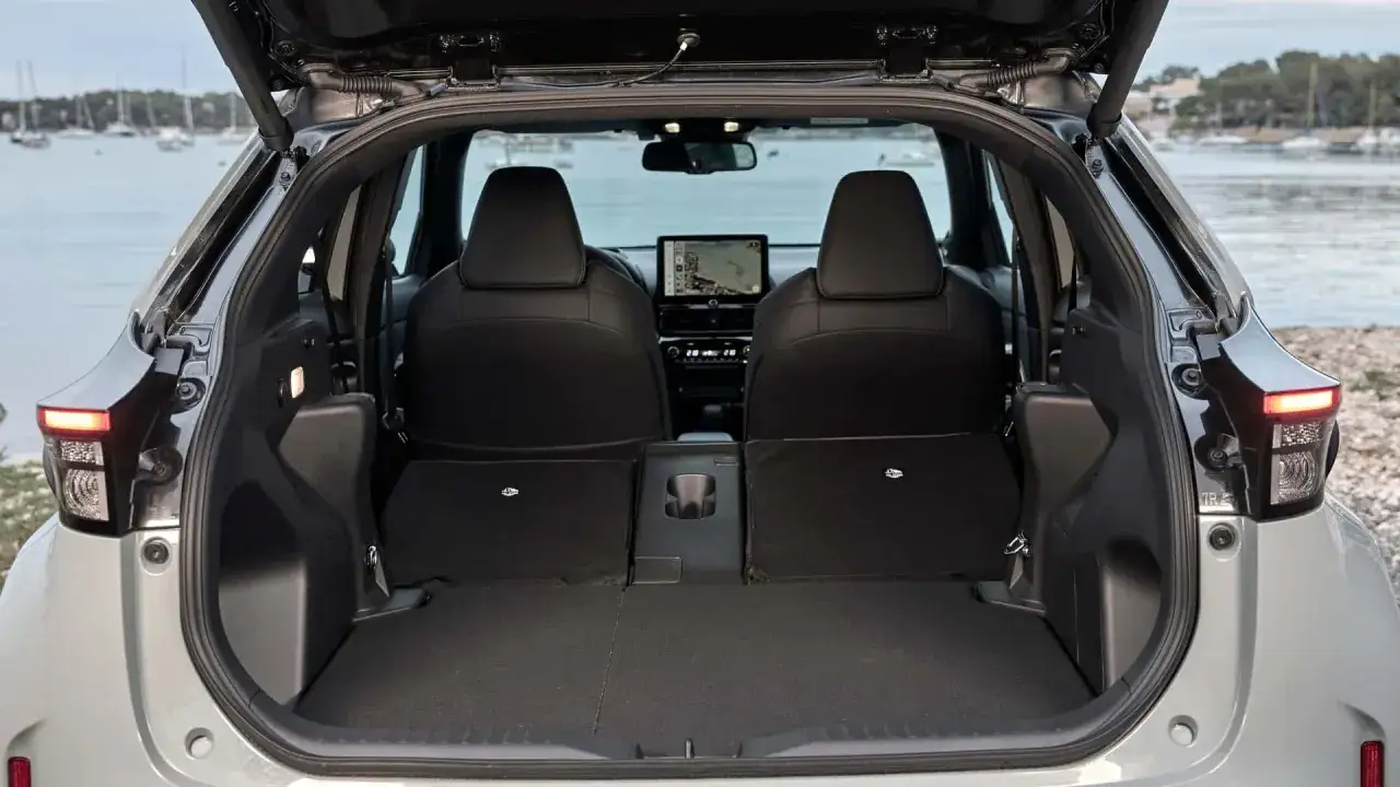 Bagagliaio aperto della Toyota Yaris Hybrid, con sedili posteriori abbassati. Dettagli interni e navigatore visibili.