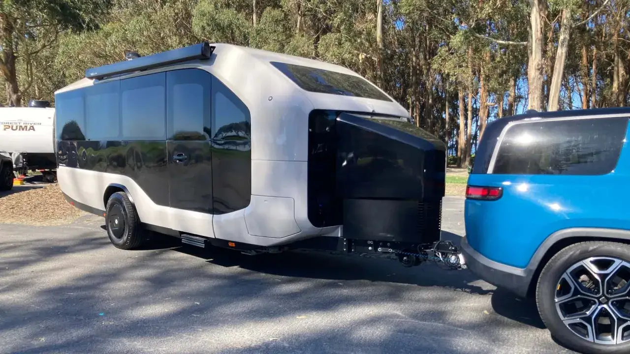 Un moderno camper elettrico, dal design futuristico, trainato da un SUV blu. Pronto per un'avventura ecologica.