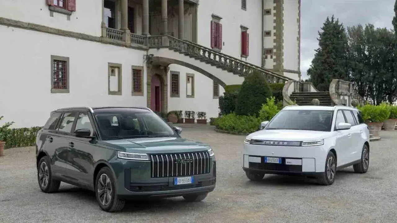 Due sport utility vehicle, uno verde e uno bianco, parcheggiati davanti a una villa storica con una scalinata imponente.