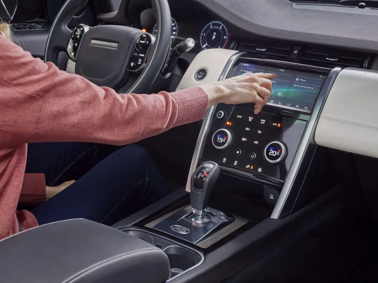 Interno di un Discovery Sport, con una mano che interagisce con il touchscreen. Nonostante la tecnologia, alcuni difetti di progettazione persistono.