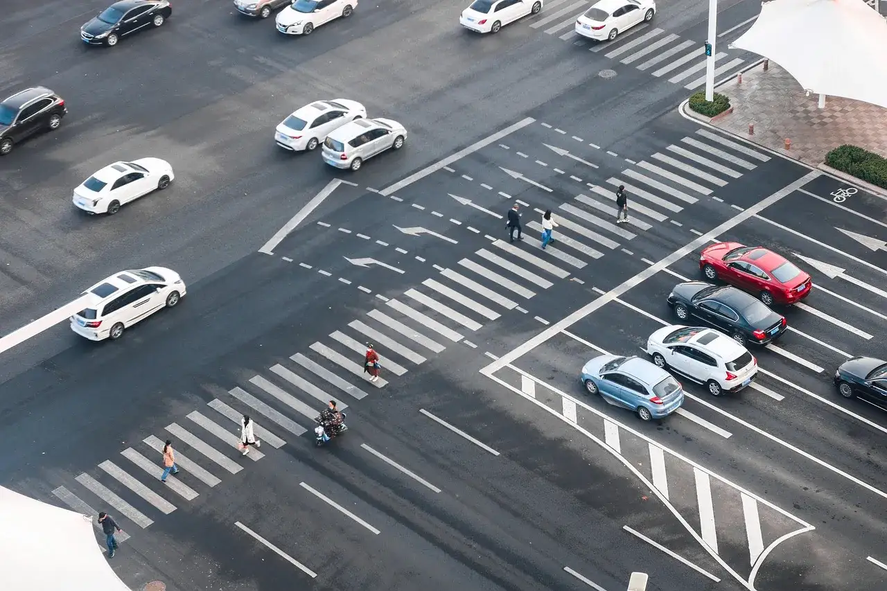 Incrocio trafficato con auto e pedoni che attraversano le corsie di canalizzazione.