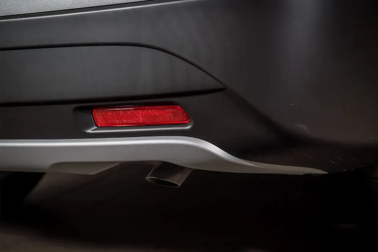 Parte posteriore di un'auto con un catadiottro rosso integrato nel paraurti. Questi catadiottri cosa sono? Sono dispositivi di sicurezza che riflettono la luce.