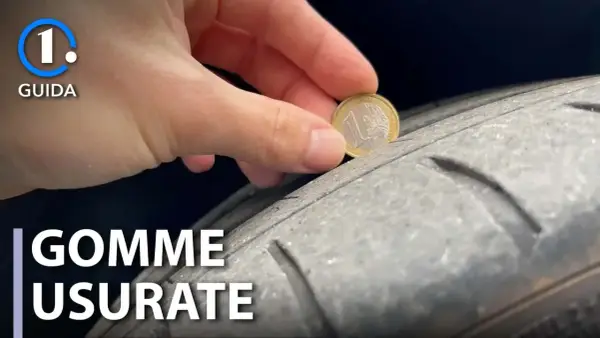 Una mano inserisce una moneta da 1 euro in un solco di uno pneumatico per mostrare come vedere se le gomme sono consumate.