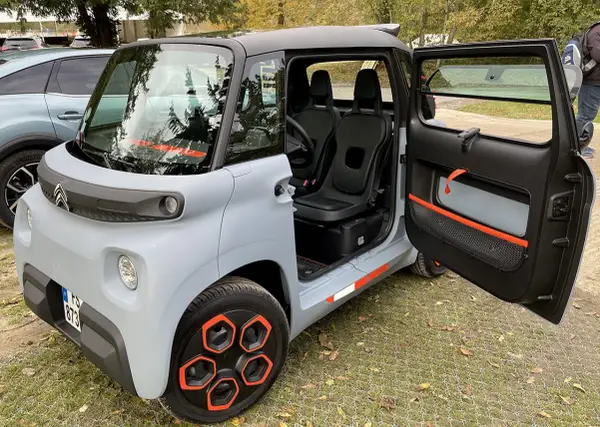 Un'auto elettrica due posti grigia con dettagli arancioni, porte aperte, sedili neri e cerchi distintivi.