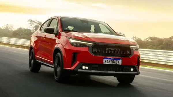 La Fiat Fastback 2026 rossa sfreccia su una pista, con il sole che illumina il cielo.