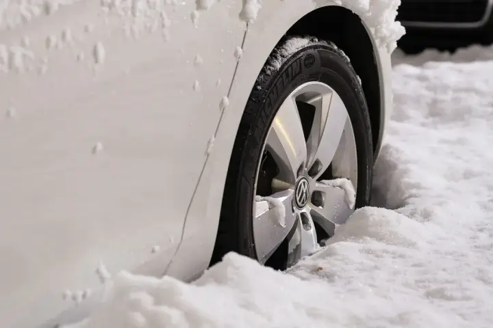 Ruota di un'auto bianca sommersa dalla neve. Il freno a mano ghiacciato rende difficile muoversi.