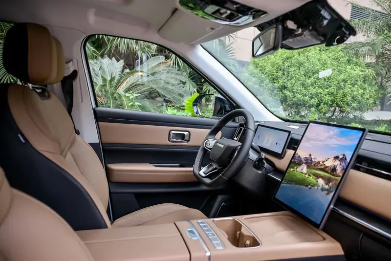 Interni del Jaecoo 7: sedili in pelle beige e nera, volante moderno e un grande schermo centrale con paesaggio montano.