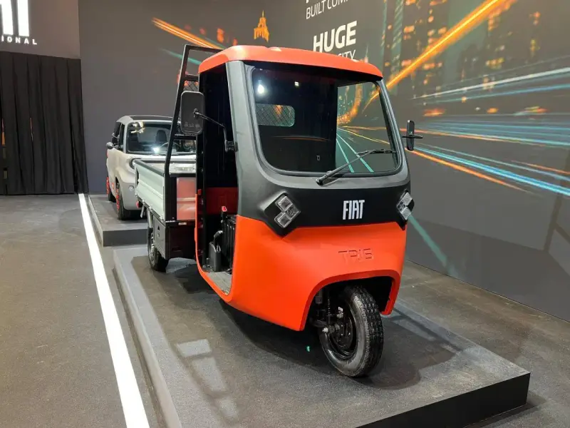 Un vivace Fiat Tris arancione e grigio, un veicolo a tre ruote per il trasporto merci, esposto su una pedana.