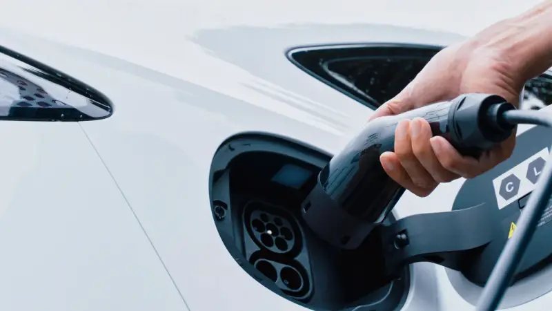 Mano inserisce la spina per trasformare l'auto in elettrica. Ricarica di un veicolo a zero emissioni.